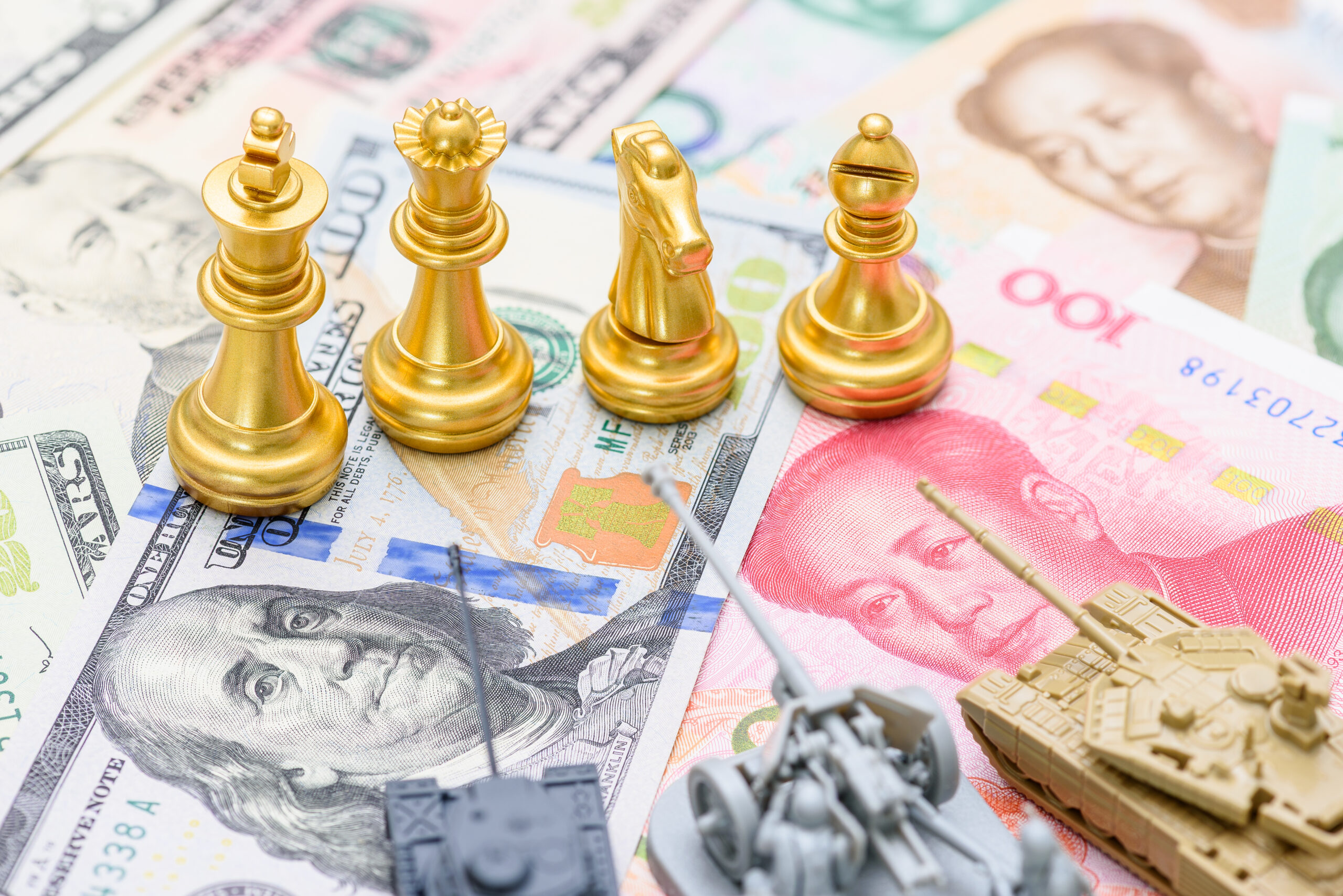 Bilateral trade agreements, economic resilience, trade and tariff war : Golden chess pieces and miniature military vehicles positioned on US dollar and Chinese yuan banknotes, US-China trade talks.
