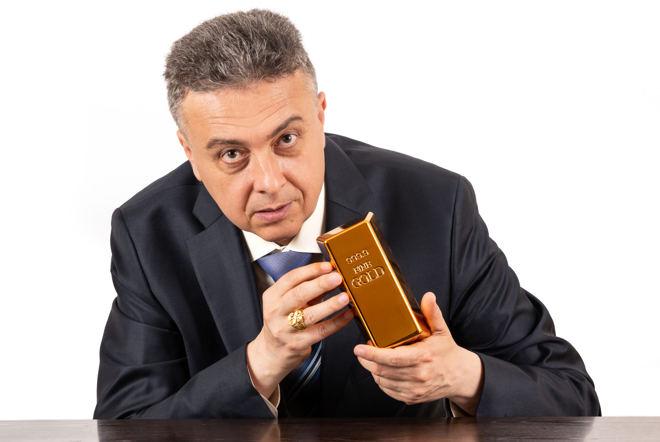 A middle-aged man in a business suit holds a 999 fine gold bar in his hands